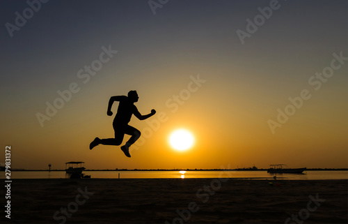 Silhouette of athletic running on the sun rise beach.