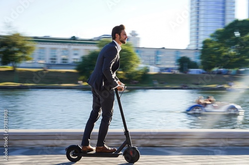 Fototapeta Young business man in a suit riding an electric scooter on a business meeting