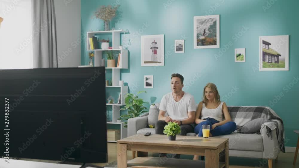 Young couple watching sports on tv on a couch in a cozy living room Young couple watching sports on tv on a couch in a cozy living room