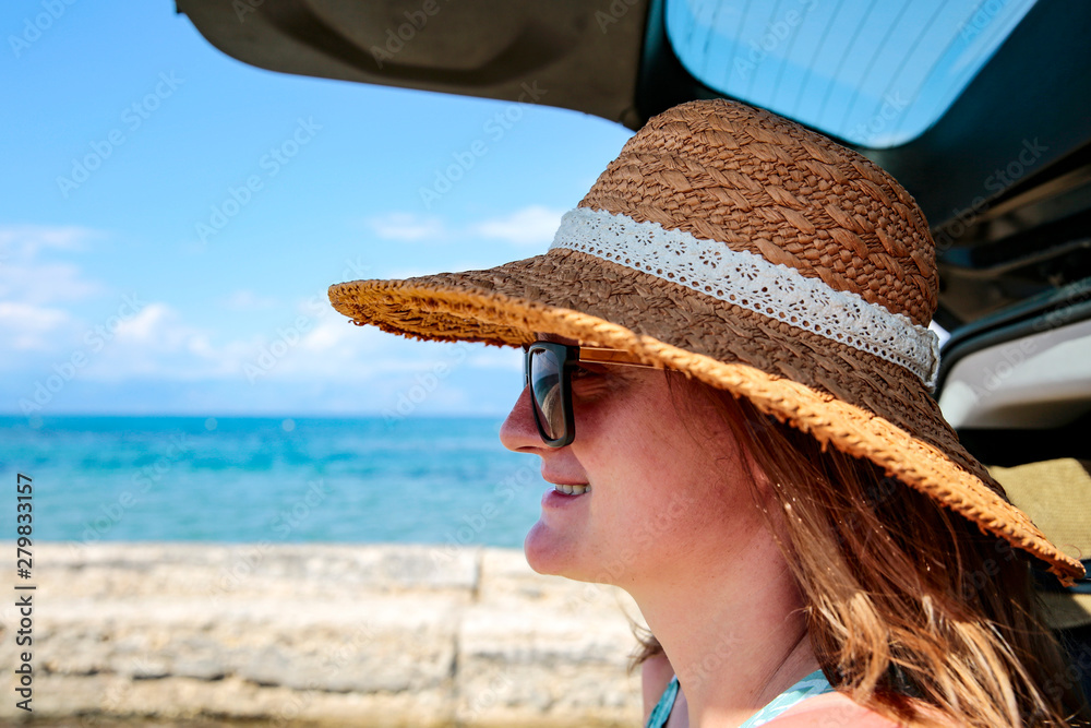 Happy woman in a hat and a summer car on the sunny sandy beach.