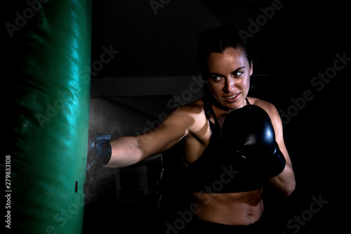 Young female boxer punching a bag on a sports training in a gym.