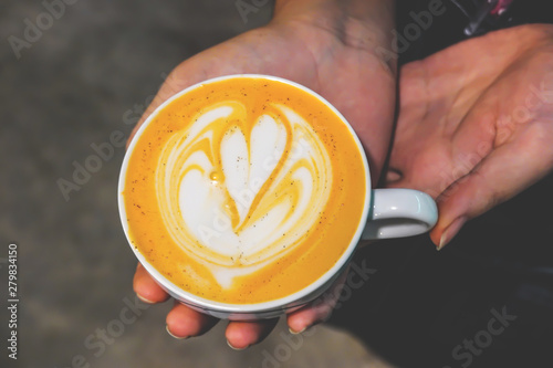 Close up image of a hand woman holds a coffee with a heart foam top view in coffee shop.