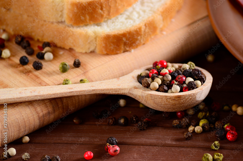 Set of black, pink, white and green pepper corns in wooden spoon on bamboo board and sliced toast bread. Mixed colorful peppercorns spieces.