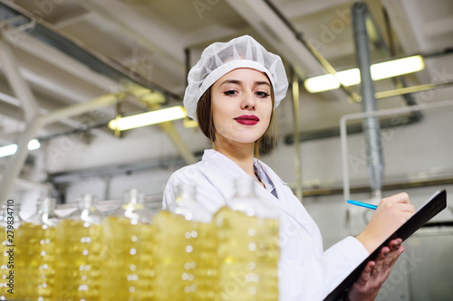 beautiful young girl is making notes on a sheet of paper on the background of a line on food production of sunflower oil.