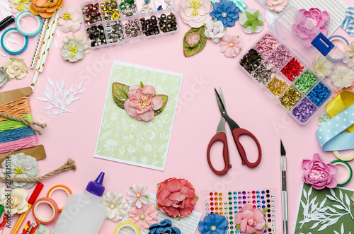 Paper flowers, scissors, homemade card, paper and scrapbooking items on pink background. Scrapbooking, top view