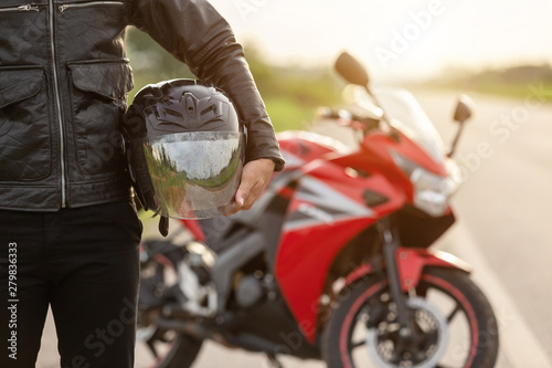 Valokuva Handsome motorcyclist wear leather jacket and holding helmet on the road