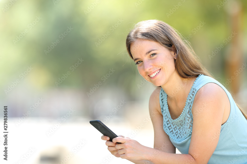 Happy woman holding smartphone looks at camera Happy woman holding smartphone looks at camera