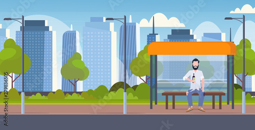 poor man drunk beggar sitting on public transport station holding bottle of alcohol homeless jobless concept city street cityscape background horizontal flat full length