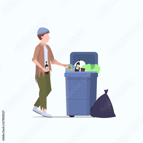 poor man beggar holding bottle of alcohol tramp searching food and clothes in trash can on street homeless jobless unemployment poverty concept white background full length