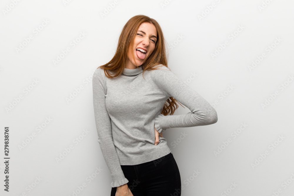Redhead girl over white wall showing tongue at the camera having funny look