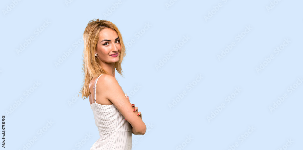 Young blonde woman with arms crossed and looking forward over isolated blue background Young blonde woman with arms crossed and looking forward over isolated blue background