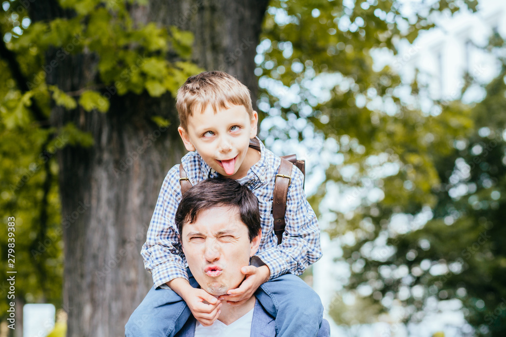 Never too old for fooling around. Portrait of playful and immature funny cute father and son squinting folding lips and showing tongue aping over big tree outdoor at summer park. Never too old for fooling around. Portrait of playful and immature funny cute father and son squinting folding lips and showing tongue aping over big tree outdoor at summer park.