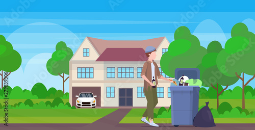man beggar holding bottle of alcohol tramp searching food and clothes in trash can on street homeless jobless unemployment poverty concept cottage building countryside background full length