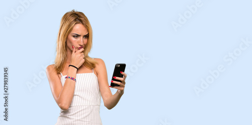 Young blonde woman thinking and sending a message over isolated blue background