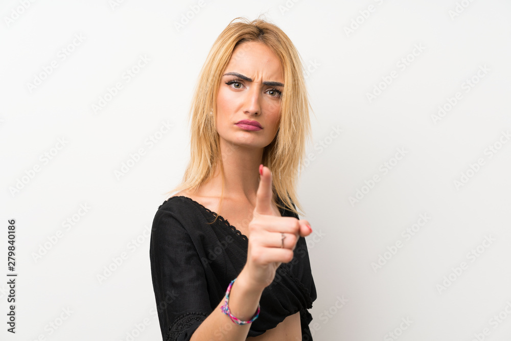 Young blonde woman over isolated white wall frustrated and pointing to the front Young blonde woman over isolated white wall frustrated and pointing to the front