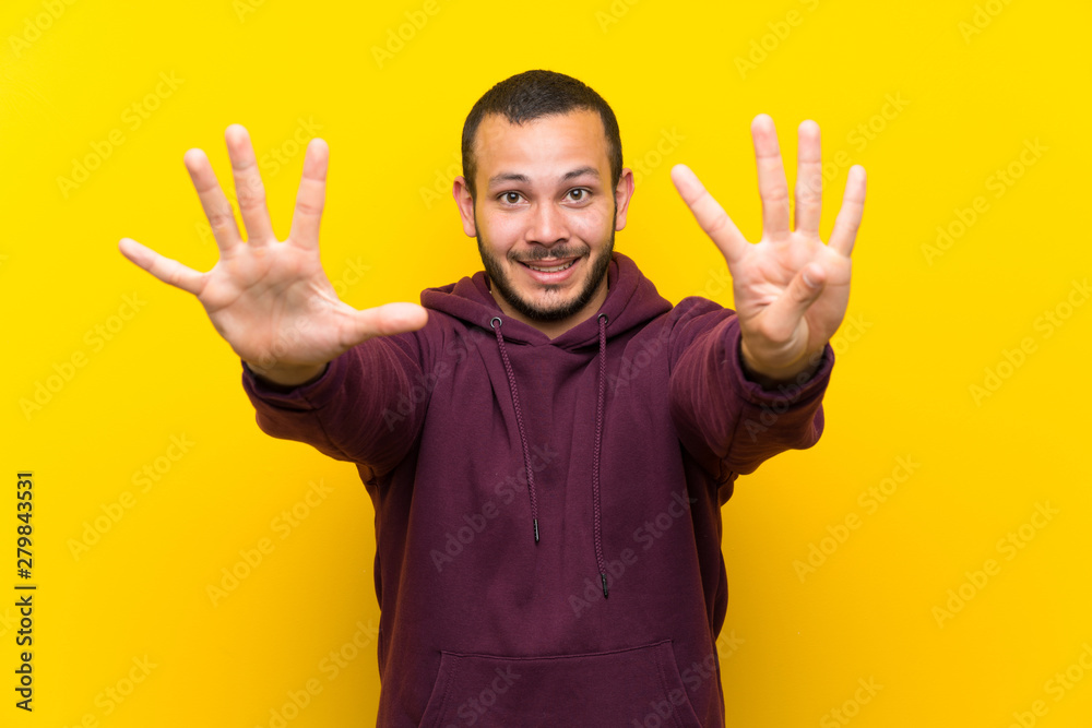 Colombian man with sweatshirt over yellow wall counting nine with fingers Colombian man with sweatshirt over yellow wall counting nine with fingers