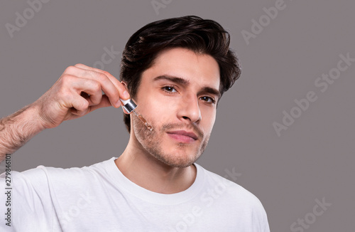 Young man applying organic essential serum on face