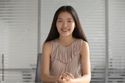 Happy smiling asian businesswoman looking at camera sit at desk