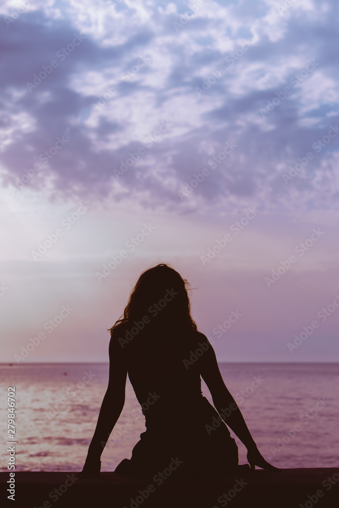 woman silhouette sitting on the beach looking at sunset over the sea