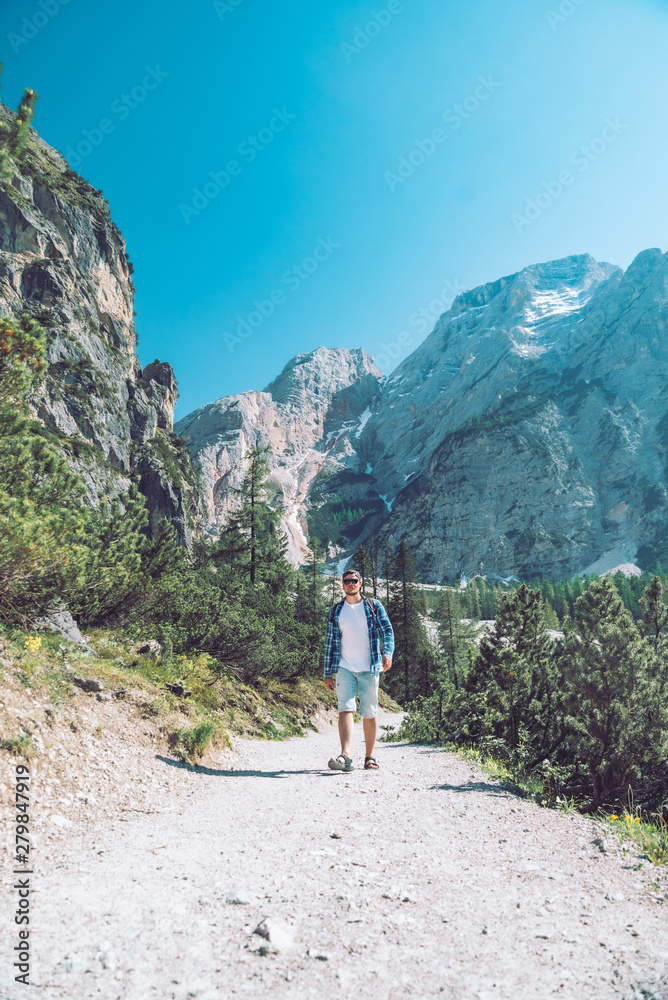 young man with backpack walking by mountains trail in sunny day young man with backpack walking by mountains trail in sunny day