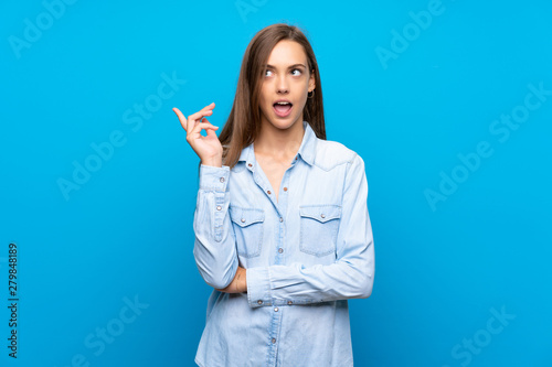 Young woman over isolated blue background thinking an idea pointing the finger up