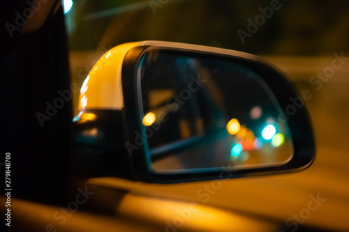 Landscape in the sideview mirror of a car , on the night road. In the side mirror of the car is reflected the lights of the night city