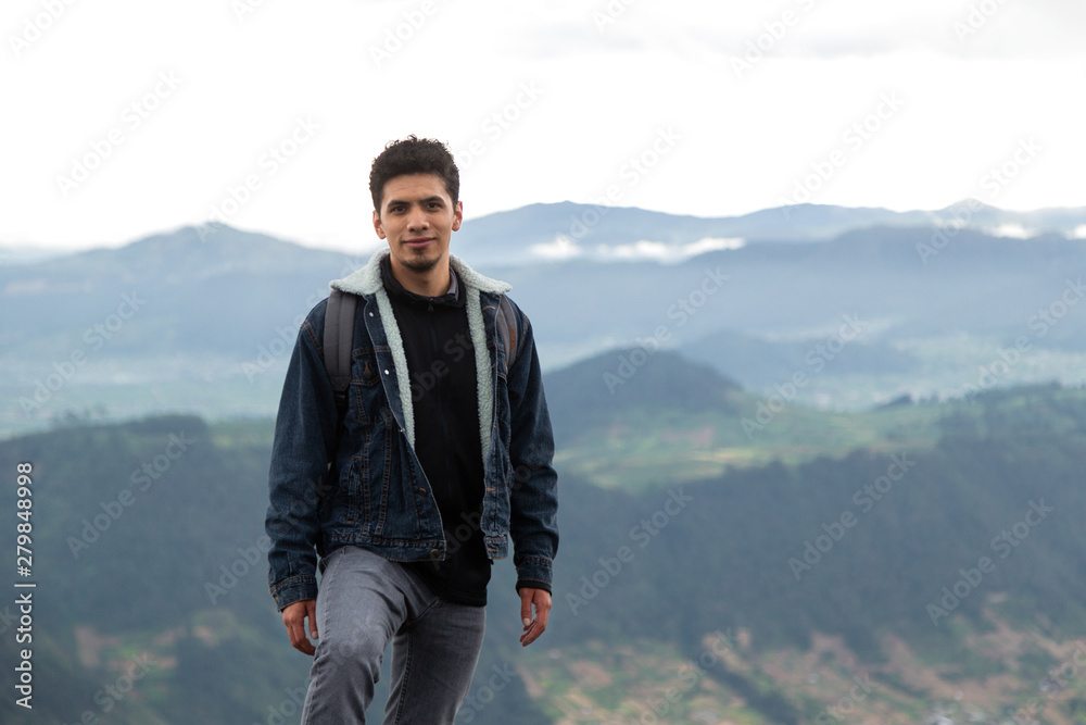 Latino man standing on top of a mountain surrounded by nature with mountains behind him- man in Guatemala
