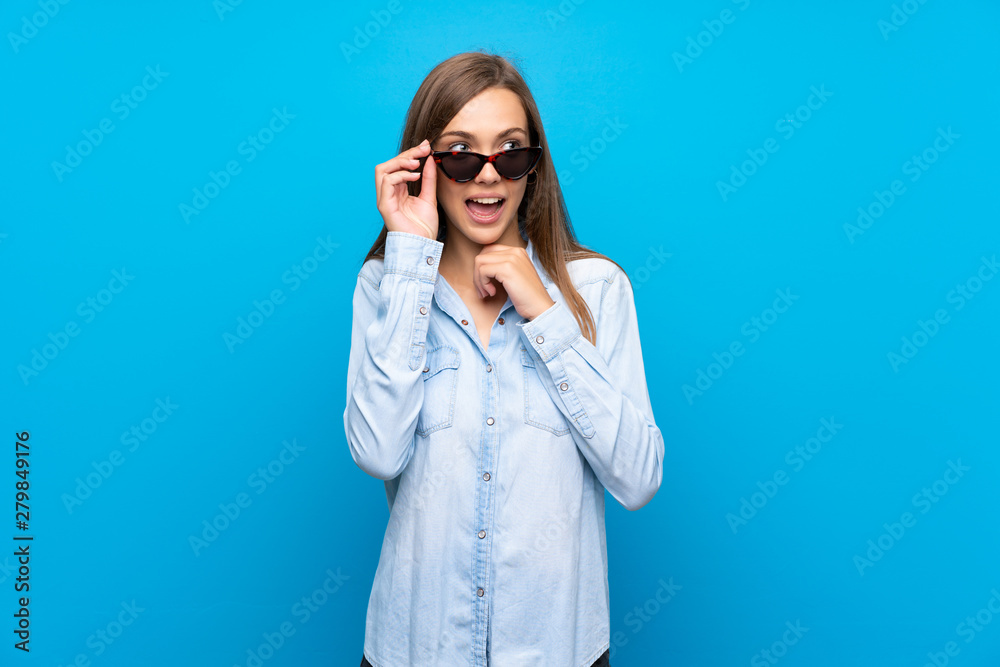 Young woman over isolated blue background with glasses and surprised Young woman over isolated blue background with glasses and surprised