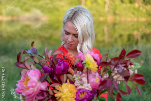Beautiful young woman with flowers in the field and a lake as a background