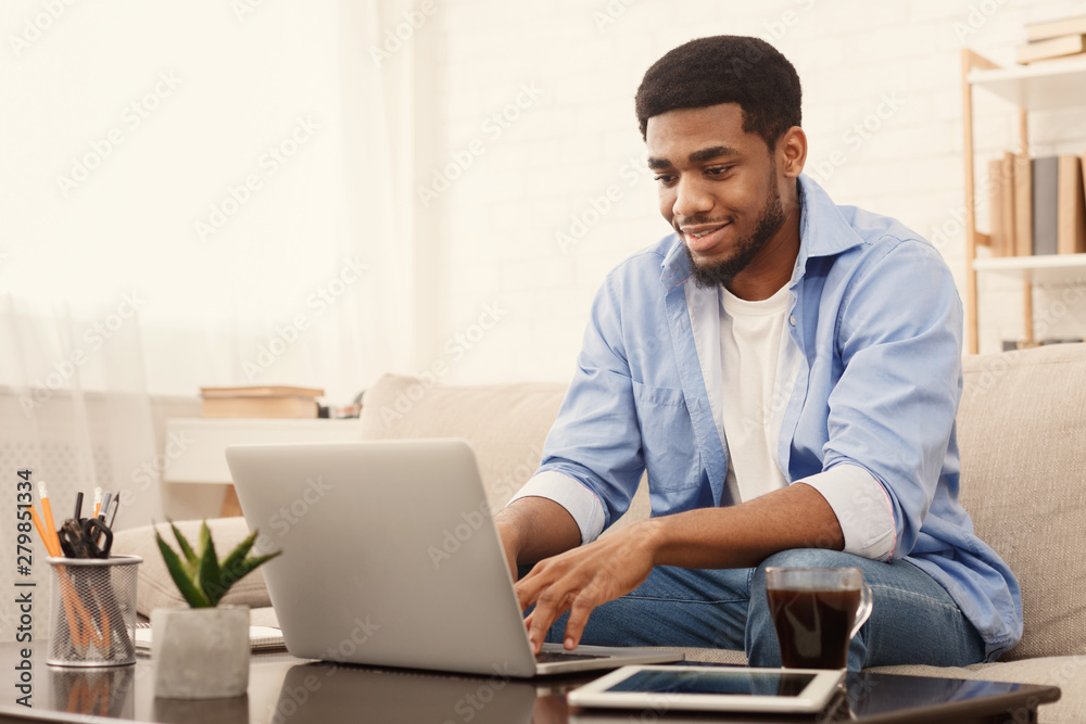 Millennial black man working on laptop in home office - obrazy, fototapety, plakaty 