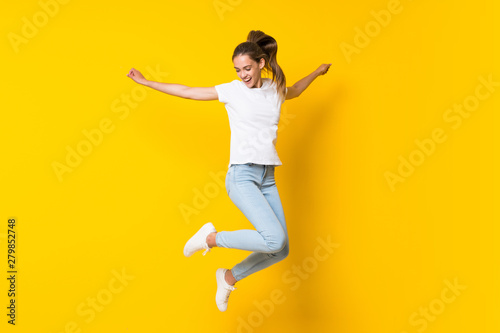 Fotografie, Tablou Young woman jumping over isolated yellow wall