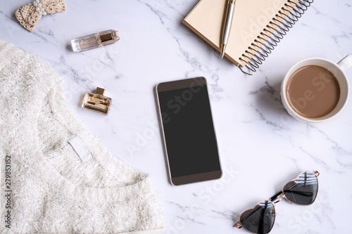 White sweater, women accessories,coffee ,notebook, smart phone on marble background top view. Women clothing. Flat lay