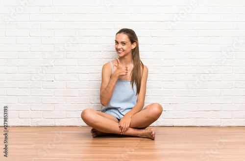 Young woman sitting on the floor giving a thumbs up gesture