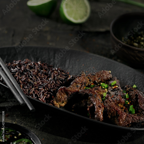 Chinese black pepper beef stir fry with black rice in a black clay plate on an old rustic table.