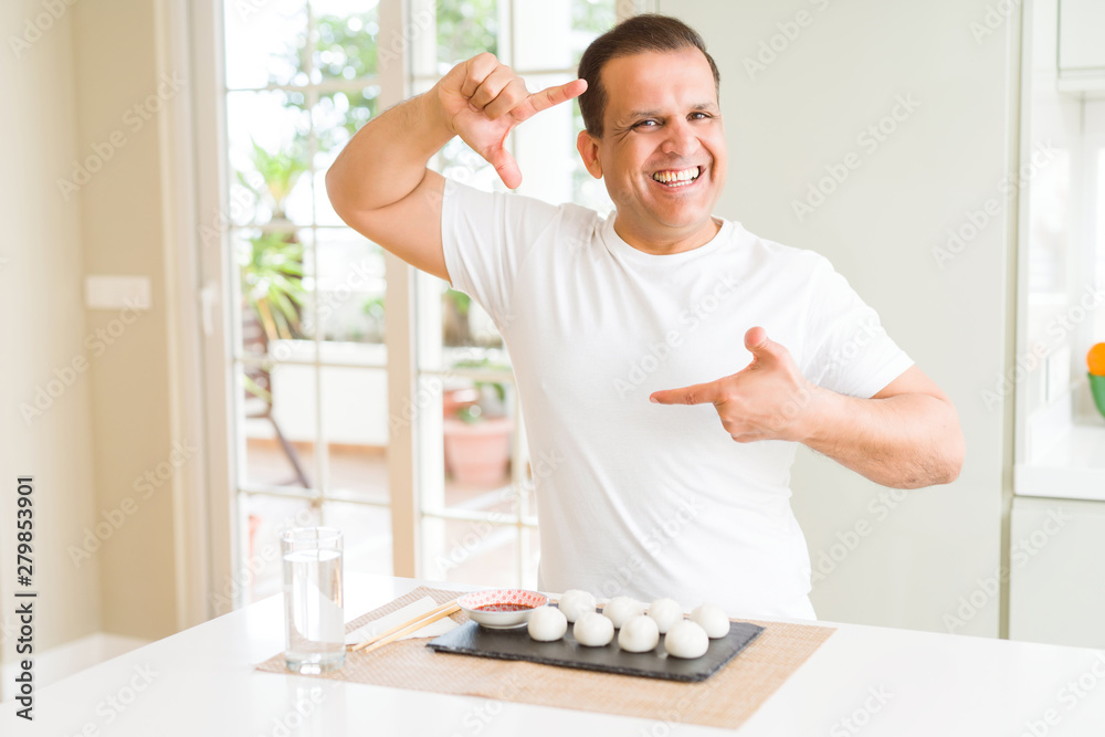 Middle age man eating asian dumplings at home smiling making frame with hands and fingers with happy face. Creativity and photography concept. Middle age man eating asian dumplings at home smiling making frame with hands and fingers with happy face. Creativity and photography concept.
