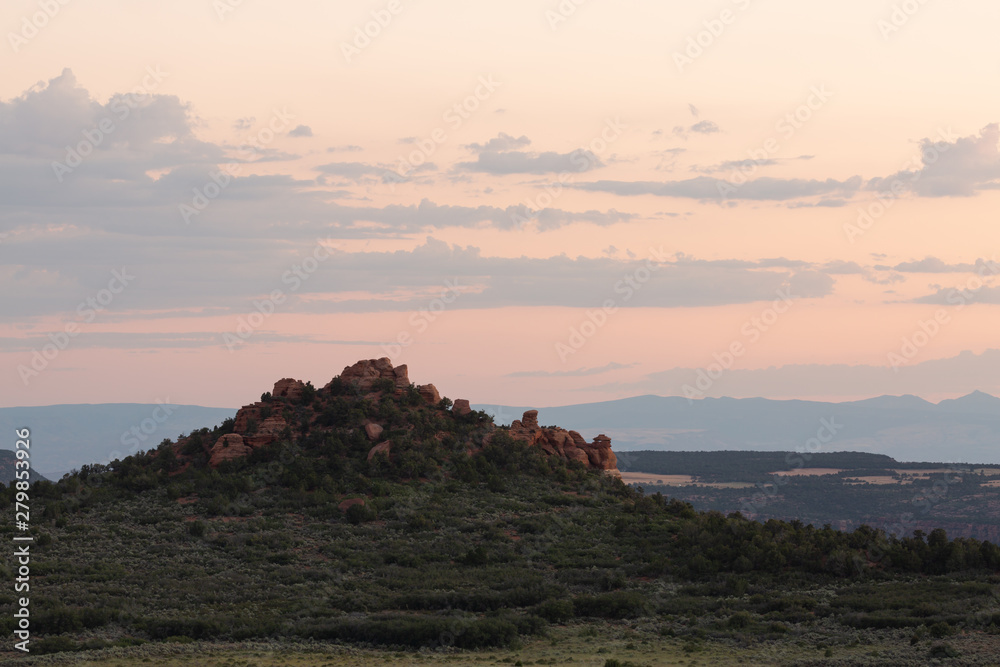 A red sandstone knoll rises up above the junipers and sagebrush in the southwest desert under a sunset sky.