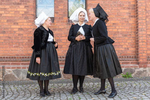 3 Wendinnen treffen sich in ihrer Kirchgangstracht vor der Kirche