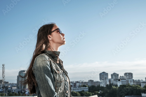 profile portrait of young girl in denim jacket and sunglasses, cityscape background