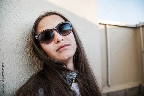 girl in sunglasses sits on floor of balcony with her head against concrete wall