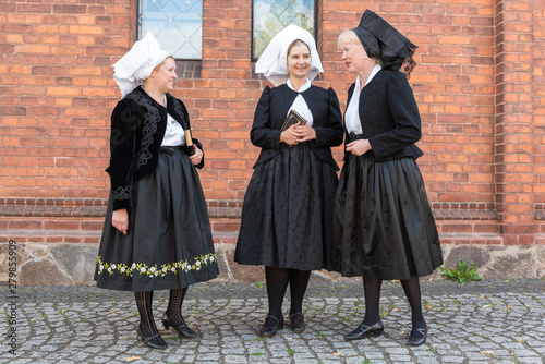 3 Wendinnen treffen sich in ihrer Kirchgangstracht vor der Kirche