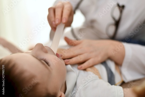 A doctor with a spatula inspects the child throat. The spatula is in the patient mouth.