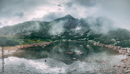 The fairy tale misty landscape the mountain Kalnate pleso lake surrounded by the mighty Tatras. Tatranska Lomnica, Slovakia. Ideal background in grey shades for the collages and illustrations.