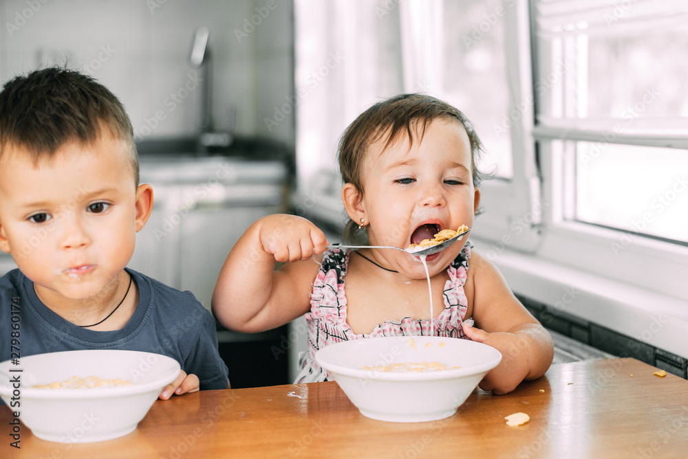 Brother and sister eat cornflakes with milk in the kitchen during the day very fun and cute, dirty and funny Brother and sister eat cornflakes with milk in the kitchen during the day very fun and cute, dirty and funny