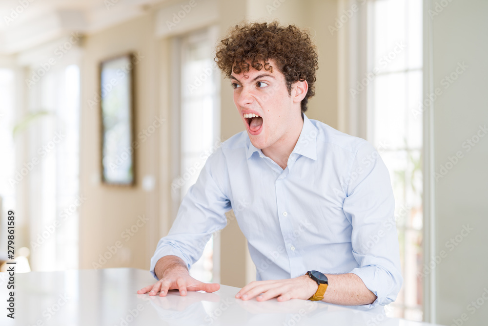 Young business man with curly read head angry and mad screaming frustrated and furious, shouting with anger. Rage and aggressive concept.