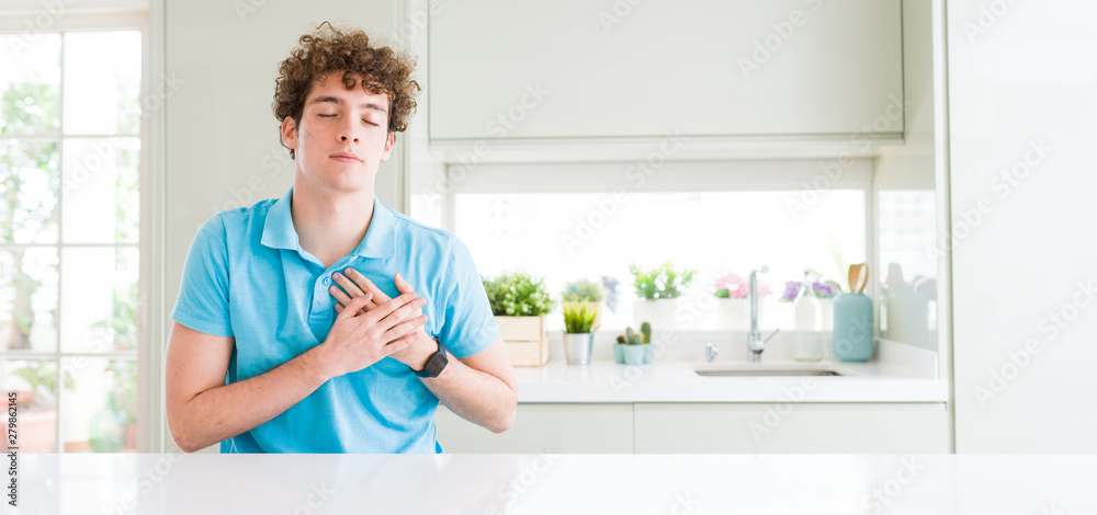 Wide shot of young handsome man at home smiling with hands on chest with closed eyes and grateful gesture on face. Health concept. Wide shot of young handsome man at home smiling with hands on chest with closed eyes and grateful gesture on face. Health concept.