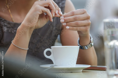 Portrait of a young beautiful woman sitting in a cafe and adding sugar in a coffee 