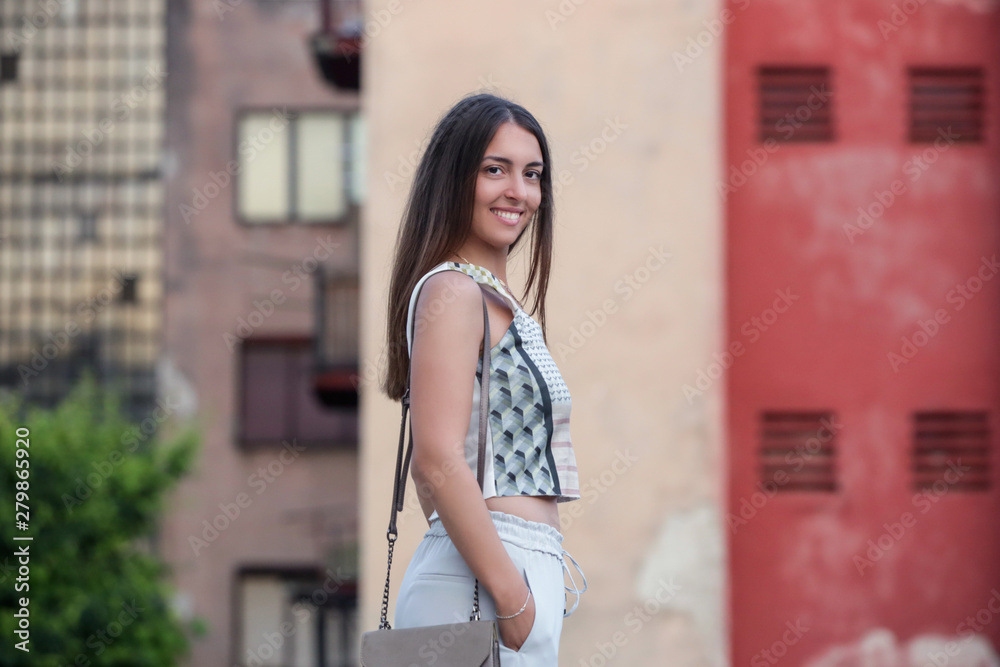 Young fashionable woman posing on the street in the front of the building facade