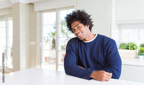 Young african american man wearing casual sweater sitting at home looking away to side with smile on face, natural expression. Laughing confident.