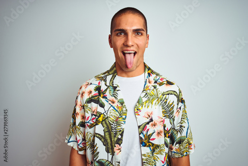 Wallpaper Mural Young handsome man on holidays wearing Hawaiian shirt over white background sticking tongue out happy with funny expression. Emotion concept. Torontodigital.ca