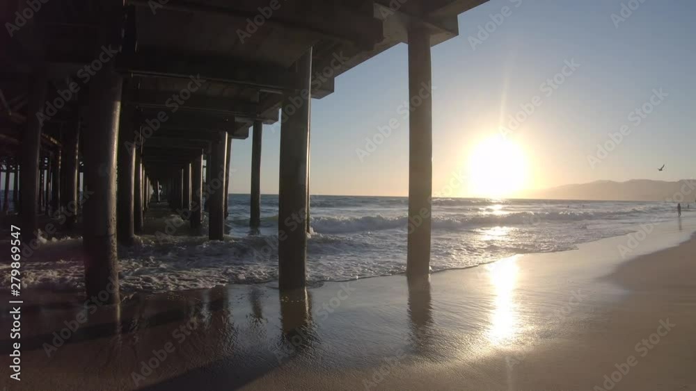 Sunset shining over gentle ocean waves on beach under wooden pier Sunset shining over gentle ocean waves on beach under wooden pier